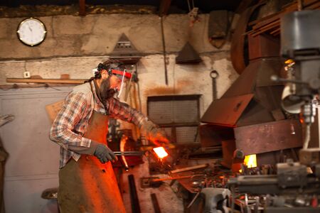 Real brutal blacksmith works in a workshop with a red-hot iron.の写真素材