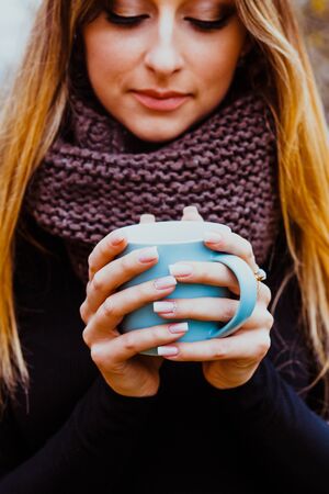 Girl enjoying hot tea outdoors in autumn day. Womens hands with perfect manicure. Autumn mood and...