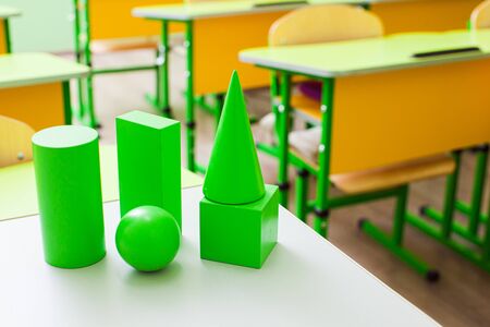 Green geometric figures of different shapes placed on a white surface. Geometry solids cube, prism, pyramid, cylinder, cone sphere in the schoolroomの写真素材
