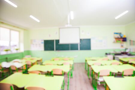 Wide angle large light schoolroom with yellow desks placed in strict rows. Chalkboard and whiteboard. Picture defocused, background for designの写真素材