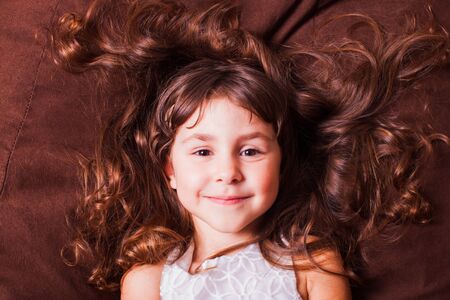 Face portrait of cute little girl with brown hair, lying on sofa. Kid dreams.の写真素材