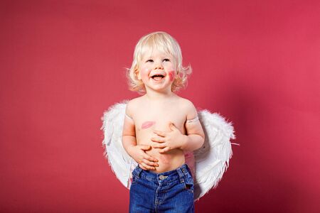 Smiling blond boy with white wings, red backgroundの写真素材