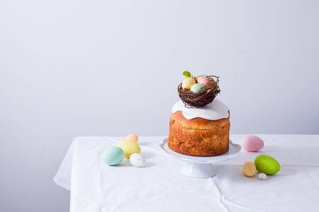 Still life holiday table with white table cloth, Easter bread on cake stand with small nest and...