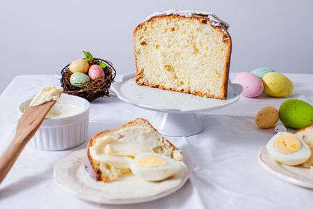 Close-up holiday served table, preparation for traditional Easter brunch. Easter cake cut into pieces, colored eggs, bowl with butter. Delicious food, eating on Easterの写真素材