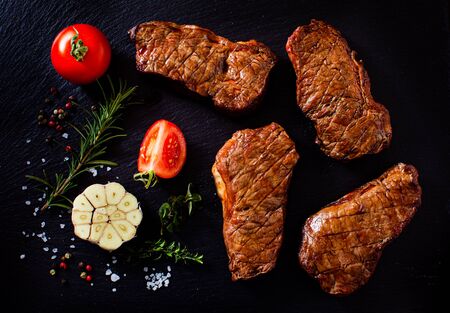 Top view of slices of a grilled steak with tomatoes, garlic and spices on a dark backgroundの写真素材