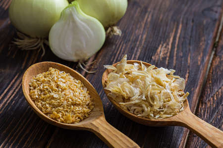 Two wooden spoons filled with seasoning made of onions, dry and ground, milled into powder and flakes. Fresh onion bulbs, cut and placed near. Wooden textured surfaceの写真素材