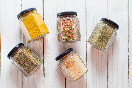 Assortment of glass jars with various ground spices and milled dry hebs. Top view on white wooden planks background.の写真素材