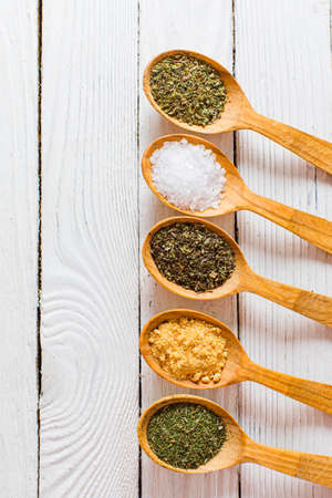 Wooden spoons with different spices, placed in straight line. Salt, mixture of herbs, ground garlic...