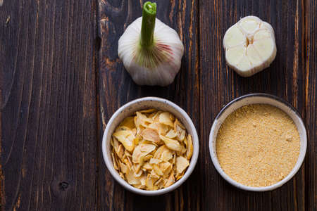Top view fresh garlic on wooden background placed near two small bowls with garlic powder and flakes. Spicy condiments for delicious dishes.の写真素材
