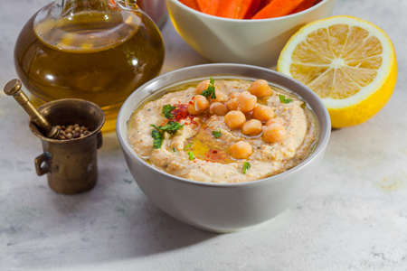 White ceramic bowl with delicious hummus spread and ingredients: chick pea, lemon, olive oil. White surface, closeupの写真素材