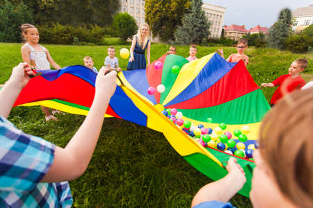 Kids holding rainbow parachute with colorful balls on itの写真素材