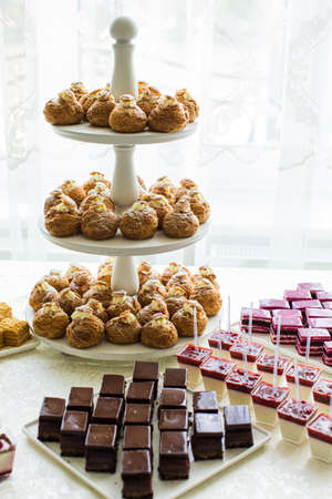 The wonderful cupcakes are laid out on a three-story white stand and many other desserts are located...