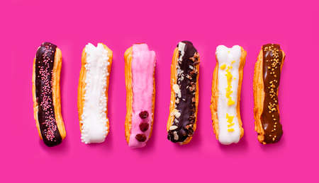 Top view of appetizing eclairs with different flavors arranged in a row isolated on the pink backgroundの写真素材