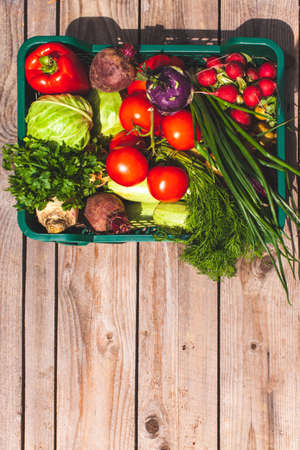 Top view of the basket is filled with various ripe vegetables on the wooden background with copyspace at the bottomの写真素材