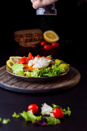 Breakfast or lunch consisting of eggs pashot style, salted salmon, avocado and lettuce. Salad and cherry tomatoes near the plate, several pieces of bread on the background. Selective focusの写真素材