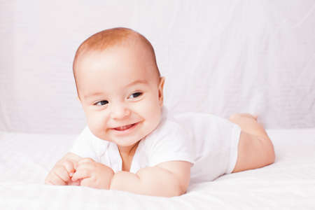 happy baby lying on white bed and smile