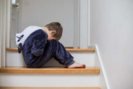 the unhappy child is sitting on the stairs with his head downの写真素材