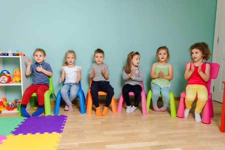 Kids are sitting on the colorful chairs, clapping handの写真素材