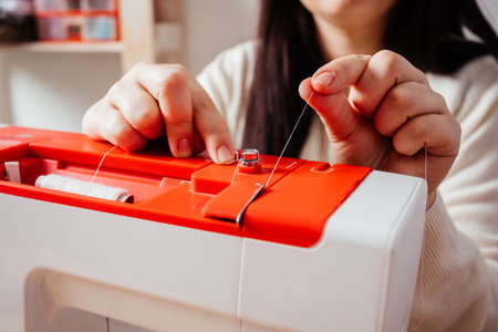 Closeup womans hands tucks the thread into the sewing machineの写真素材