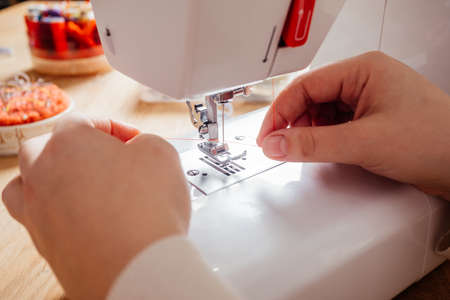 Closeup hands inserting thread into sewing machine needle