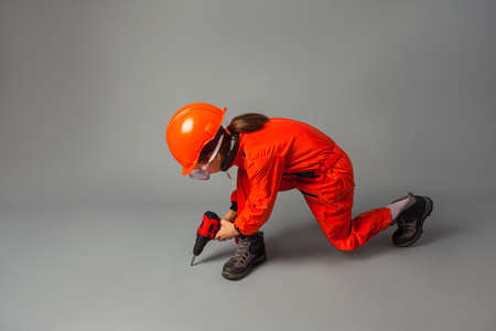 The little girl dressed in a red engineering uniform is holding a screwdriverの写真素材