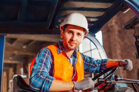 Young confident warehouse worker posing in a forklift truck