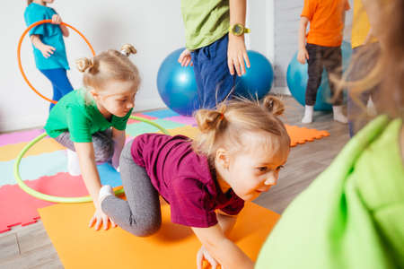 Curly girl crawling on colorful floor through hula hoopsの写真素材