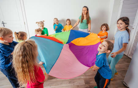 Teacher and kindergarten kids playing with colorful parachuteの写真素材