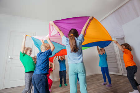Games with colorful canopy, children sitting under parachute