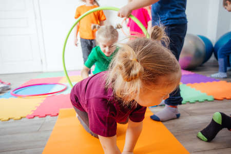 Curly girl crawling on colorful floor through hula hoops