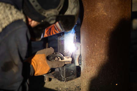 The man in uniform welds a metal at the factory