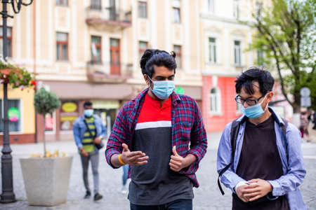 Two young multiracial friends in masks chatting outdoorsの写真素材