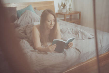 Lovely woman reading, laying on comfortable bedの写真素材