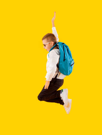 Jumping emotional schoolboy on the yellow background