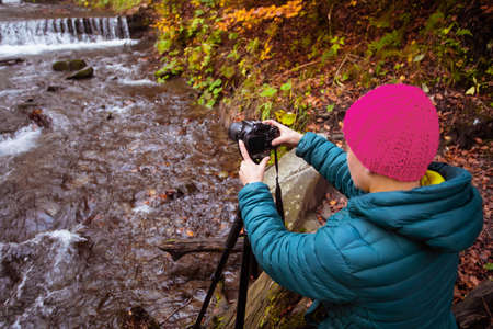 Woman photographer takes a photo forest waterfall in the autumn