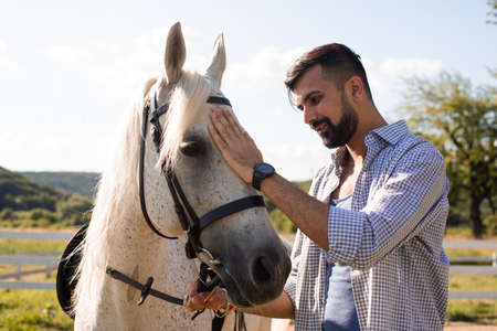The happy man is stroking a white horse in a ranchの写真素材
