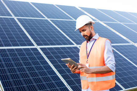 Engineer with a tablet stands on the background of a solar station