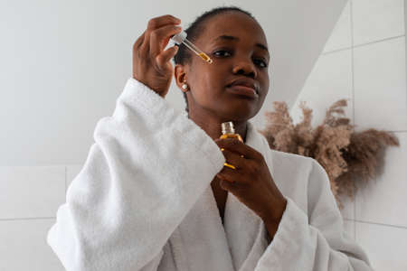 Beautiful black girl dropping serum collagen moisturizer on face