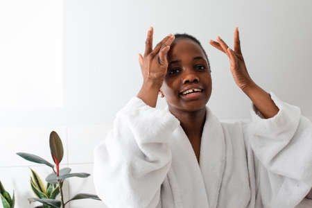 Mirror reflection portrait of girl applying serum on faceの写真素材