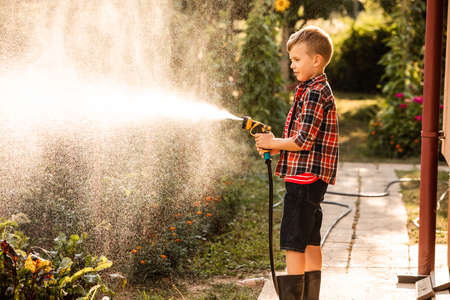 The boy is watering the garden bed using a hoseの写真素材