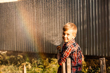 The boy enjoys a rainbow while watering in the gardenの写真素材