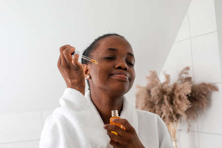 Beautiful black girl dropping serum collagen moisturizer on faceの写真素材
