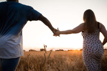 Couple holding hands while walking in fieldの写真素材