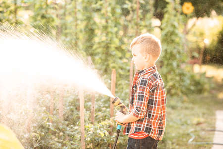 The boy is watering the garden bed using a hoseの写真素材