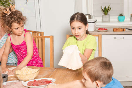 Happy kids sit at a table in the kitchen and make pizzaの写真素材
