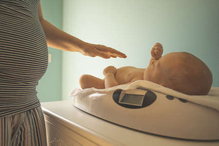 Mother weighs her newborn baby at home scalesの写真素材