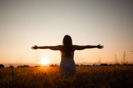 Peaceful woman wellcoming the rising sun in field