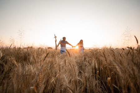 Mixed race young adult couple holding hands while walking in fieldの写真素材