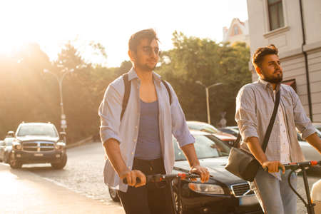 Two adult students stand in the city with electric scootersの写真素材