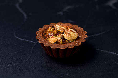 One chocolate tartalet with caramel cream and nuts on a blackの写真素材